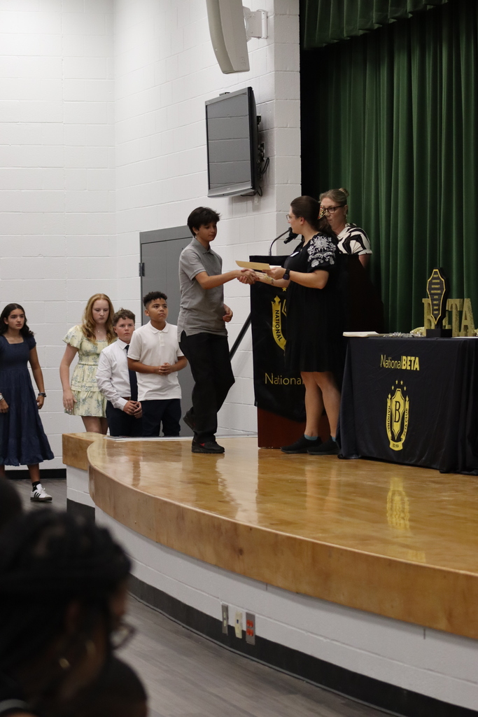 A group of people, including children, stand on a stage. A person receives an award from another.