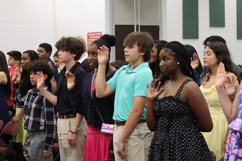 A group of students stand in a row, some raising their right hands, possibly for a pledge.