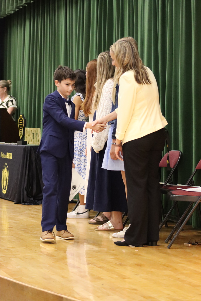 A boy in a blue suit shakes hands with a woman in a yellow top on stage.