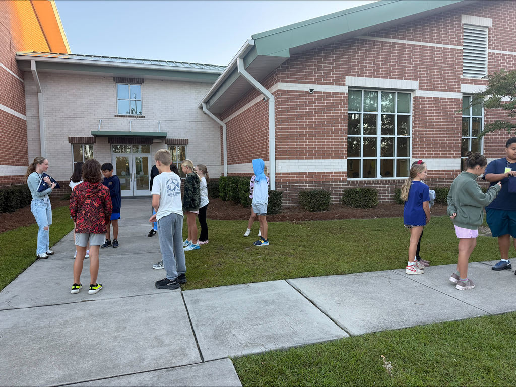 A group of young people stand on a concrete path in front of a brick building.