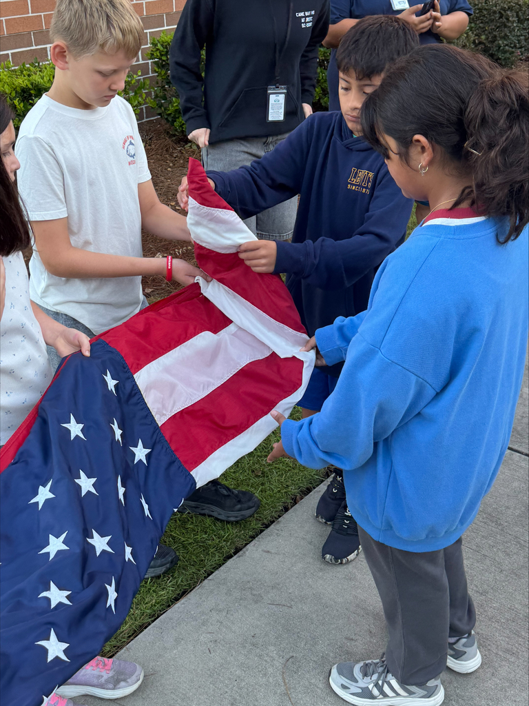 Group of children in casual clothing holding up a United States flag on a sidewalk.
