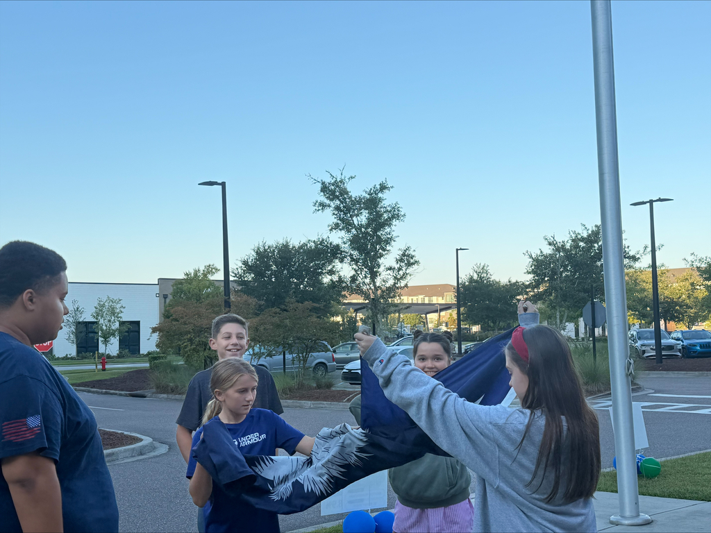 Group of people holding a flag, one with long hair, others in blue shirts, holding the flag in a parking lot.