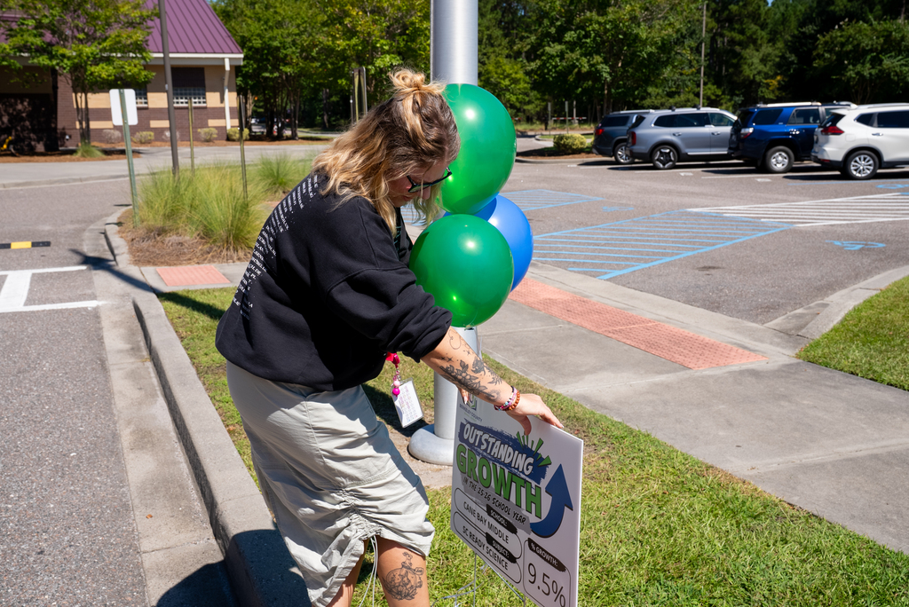 A person placing a sign with the word "Growth" near balloons. Cars parked on both sides.