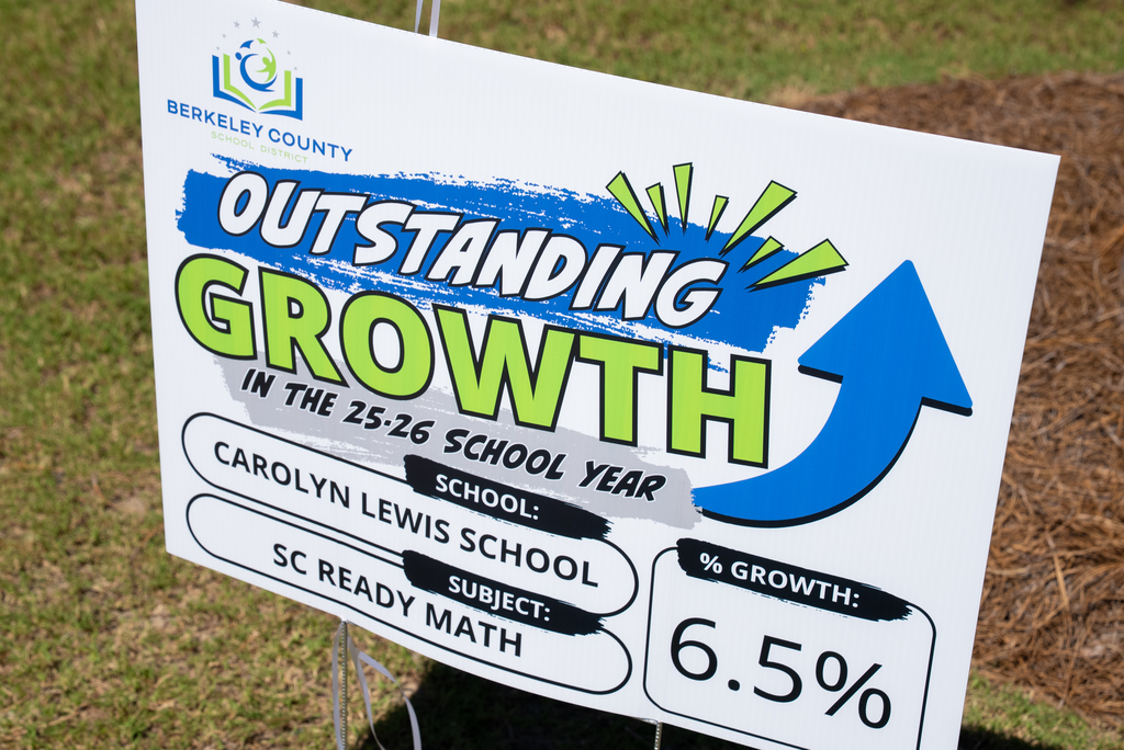 A white sign with blue and green text reads "Outstanding Growth in the 25-26 School Year." Below, it lists the school name, subject, and percentage growth.