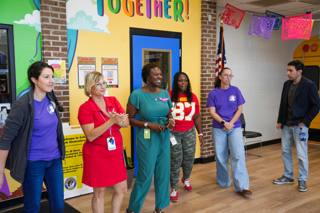 Group of adults in a colorful classroom with brick walls, a yellow wall, and bunting.