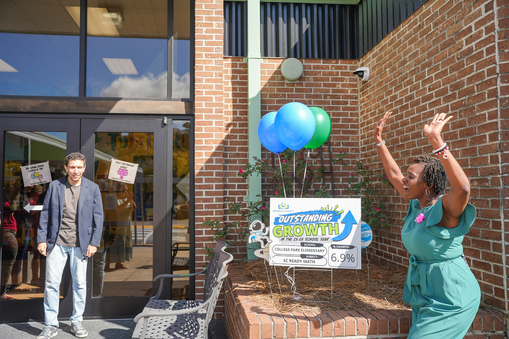 People outside a building with a brick wall. One raises hand, another stands by entrance.