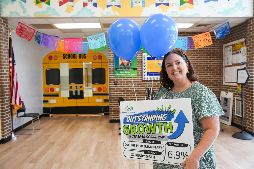 A woman in a green shirt holds a sign that reads "Outstanding Growth" with blue balloons in the background.