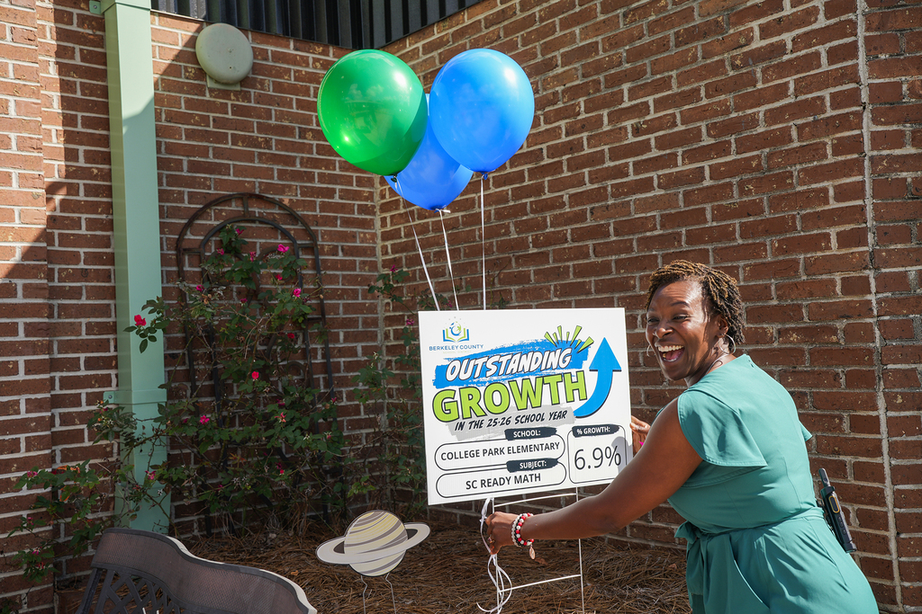 A woman in a green dress stands next to a sign reading "Outstanding Growth" with balloons and a garden.