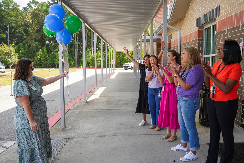 Six women on a porch. One woman holds a pole with balloons. The others clap.