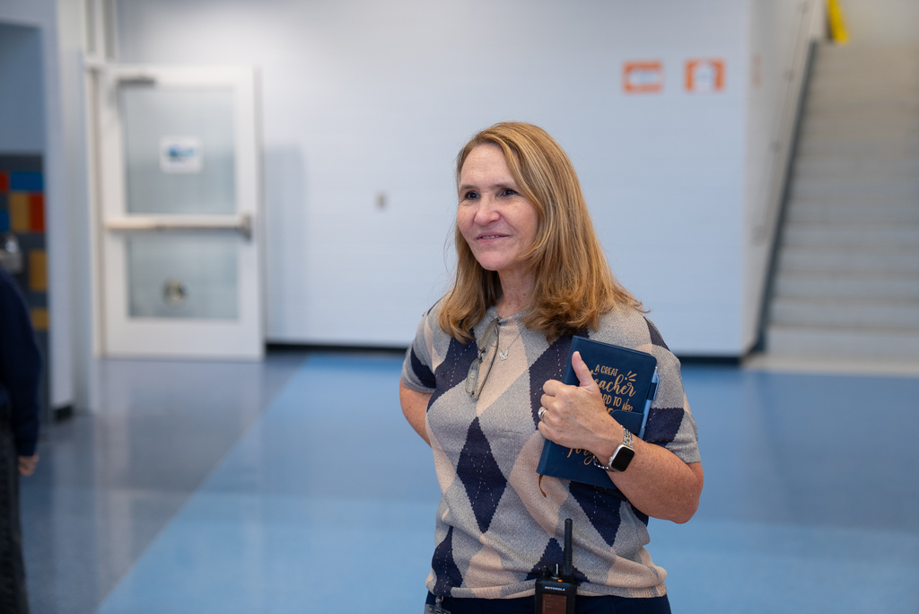 A woman with blonde hair smiles while holding a blue book and giving a thumbs up.