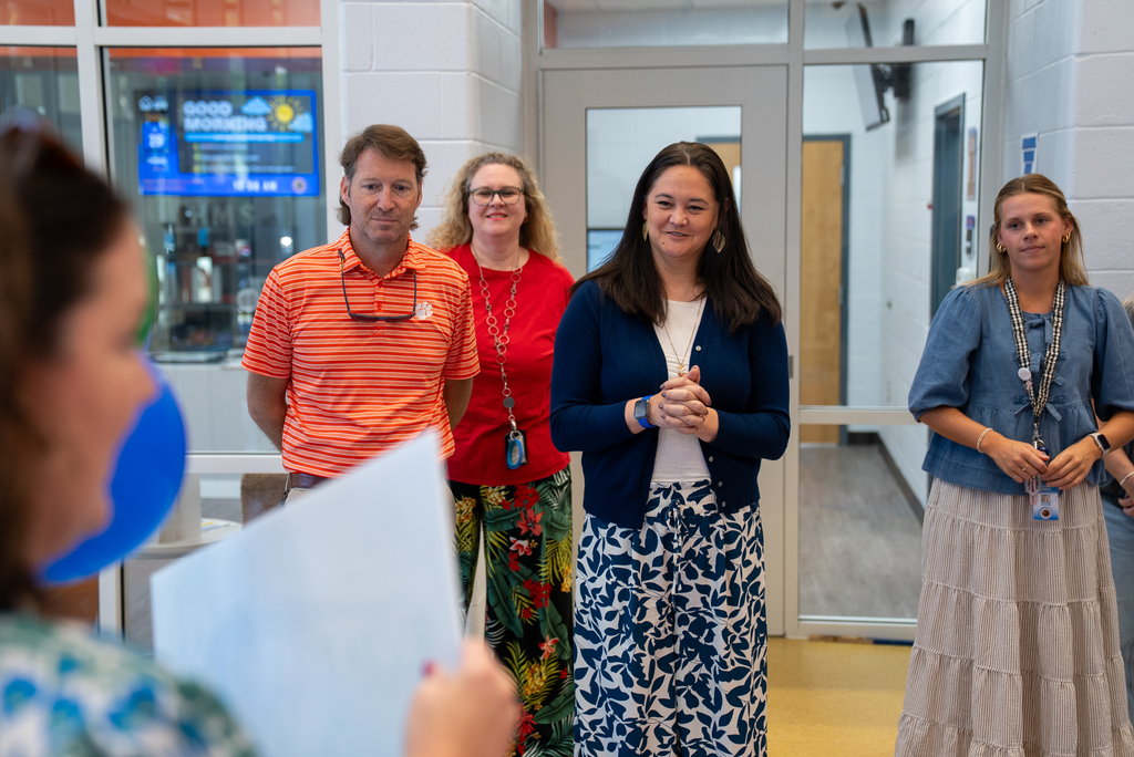 Five people, three women and two men, stand in a hallway with one woman holding paper. Behind them is a glass door.