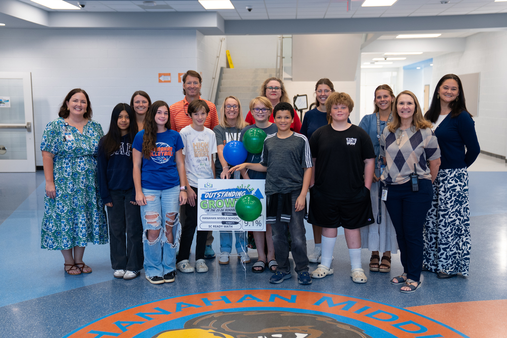 A group of people in a hallway, some holding balloons, posing for a photo. Logo on the floor reads "Manhattan Middle."
