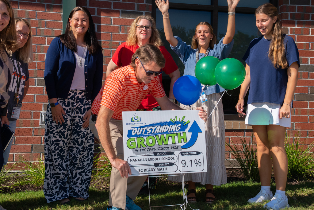 People in a brick building background. A man holds a board with "Outstanding Growth" and 9.1%.