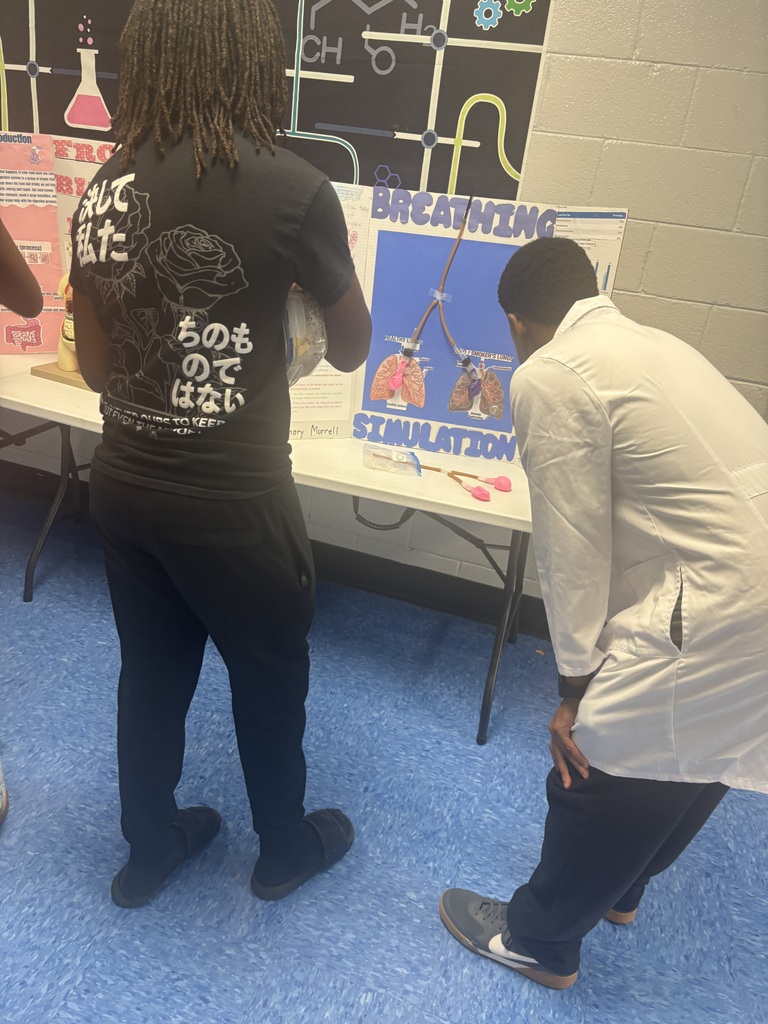 Two individuals are standing, one bent over, looking at a table displaying a sign that reads "Breathing Simulation".
