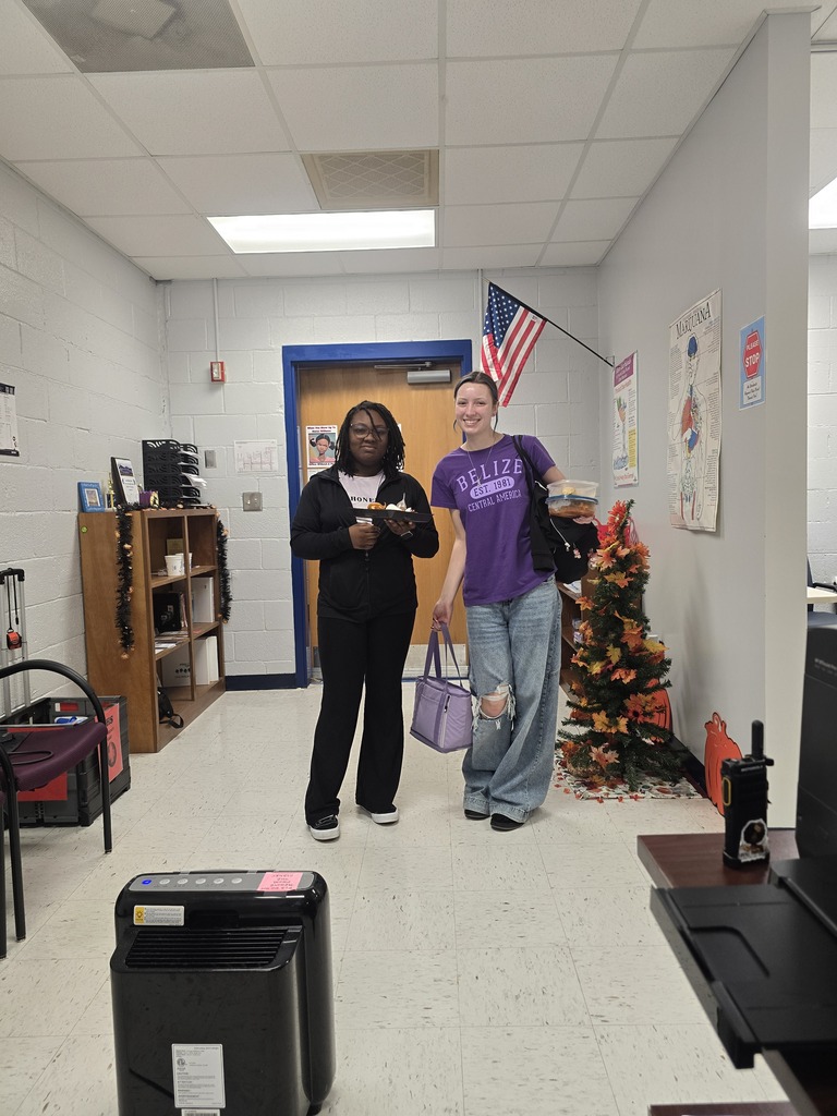 Two people stand in a hallway with a white floor and white walls. An American flag hangs on the wall.