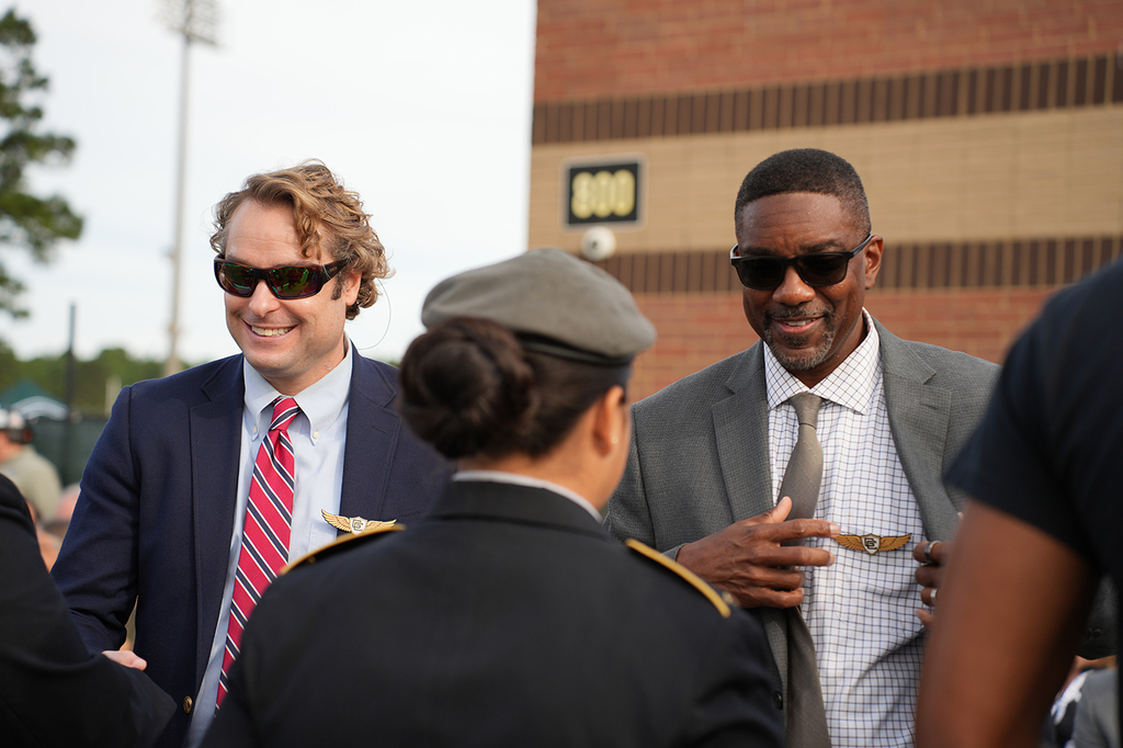 Three people conversing; one in a military uniform, another in a suit with a striped tie, and a third in a gray suit.