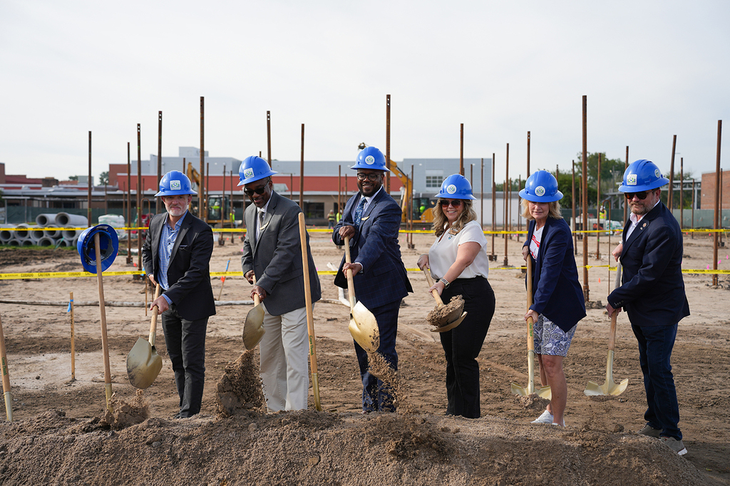 Group of people at a construction site holding shovels. The dirt is in front of them.