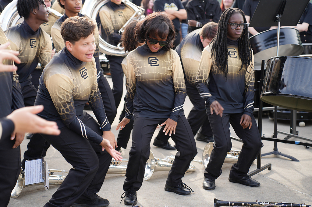 A group of people in matching uniforms, with some performing dance moves, in front of musical instruments.