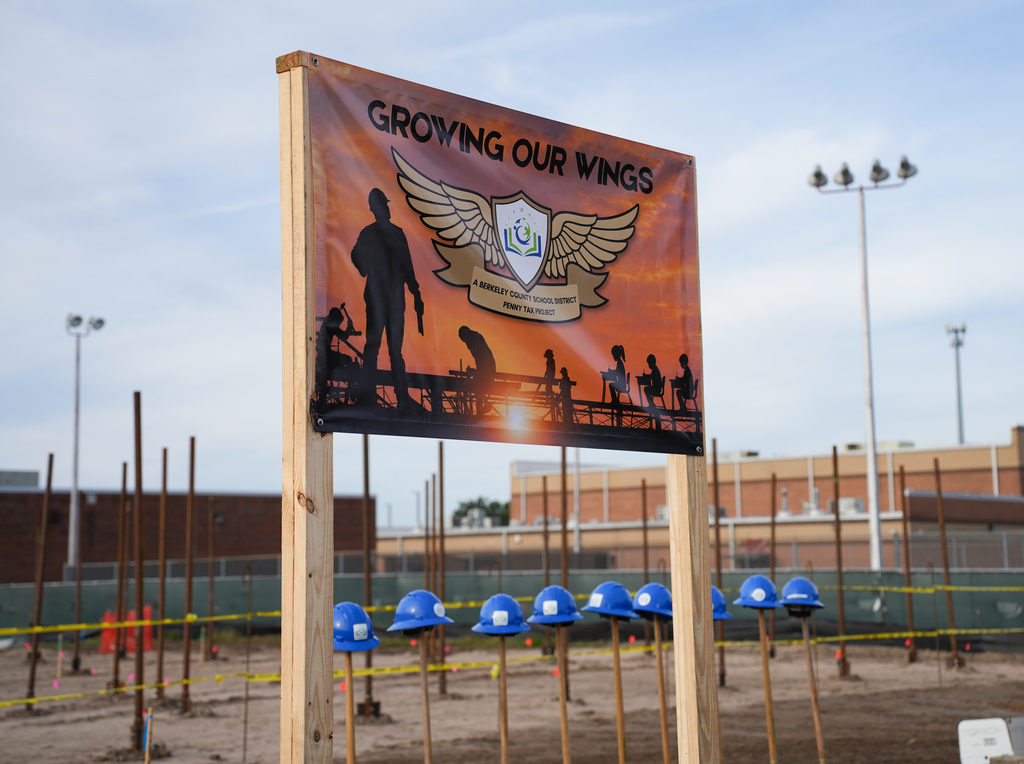 A banner reading "Growing Our Wings" on a post with a silhouette of workers. Hard hats and construction signs around.