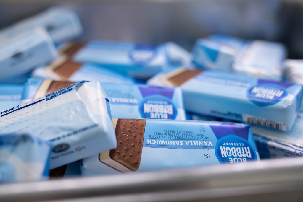 A close-up of multiple blue-and-white-wrapped ice cream sandwiches stacked in a container.