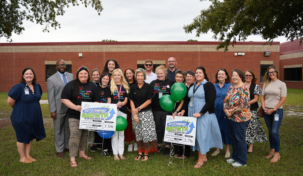A group of people stand outside a brick building with green balloons, holding signs that read "Growth".