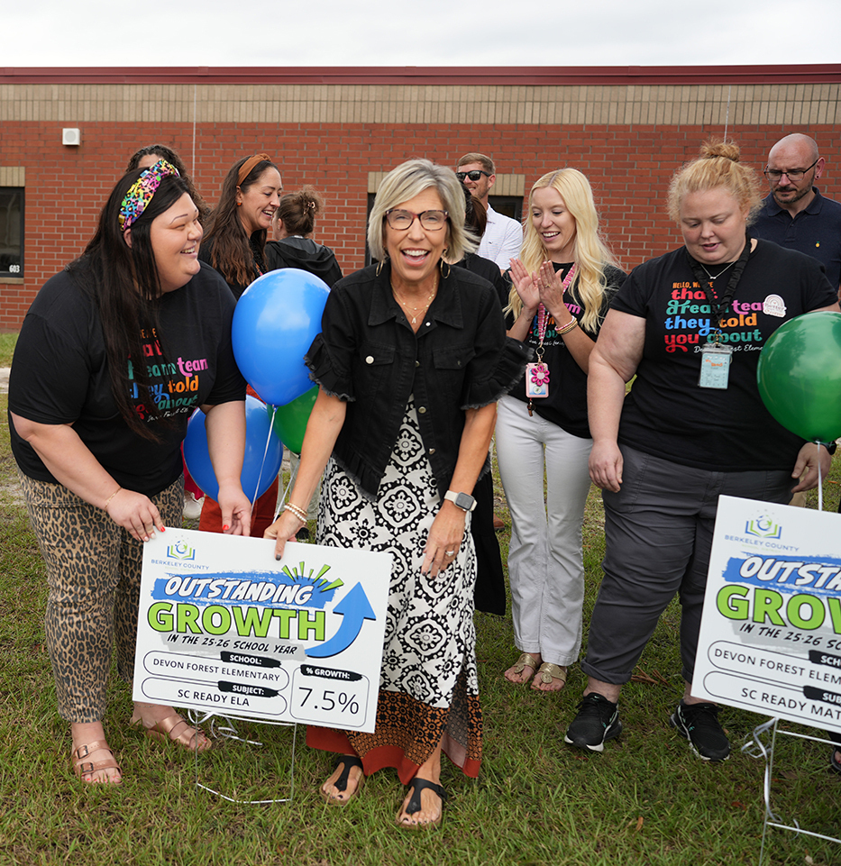 Group of adults standing outdoors. One woman holds a green sign. Sign says Outstanding Growth with a percentage.