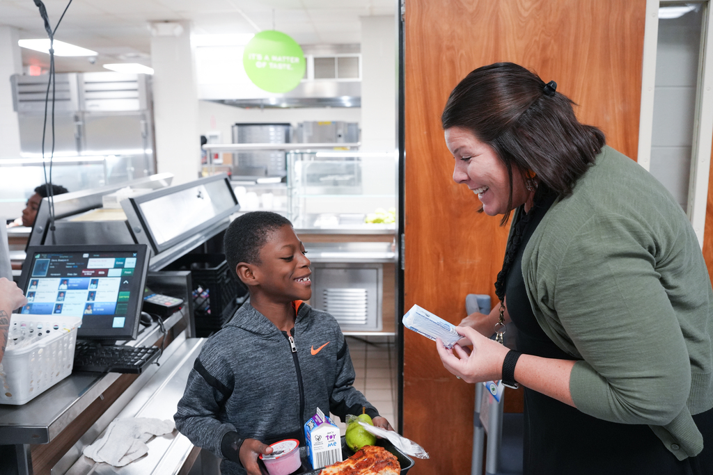 A woman with short hair smiles and holds a ticket while talking to a boy in a jacket.