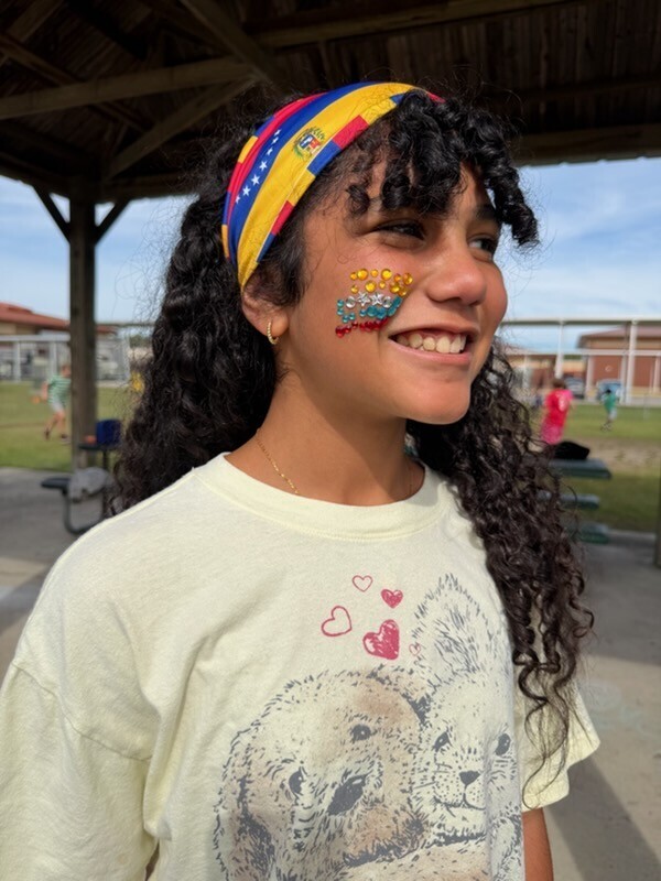 A student with a Hispanic Heritage scarf in her hair and jewels on her face. 