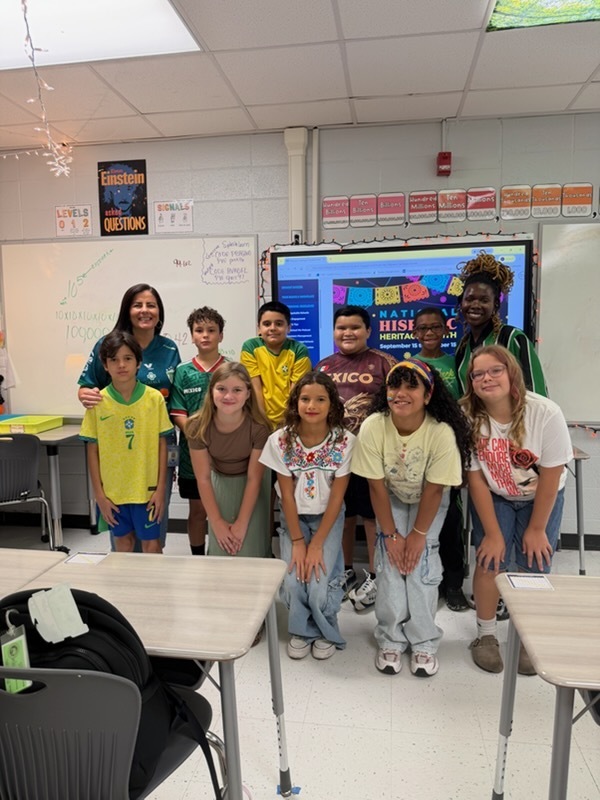 Students and adults dressed in Hispanic colors standing in front of Hispanic Heritage Month background.
