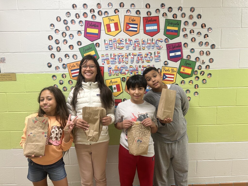 Four children pose in front of a wall with an array of flags and the text Hispanic Heritage Month.