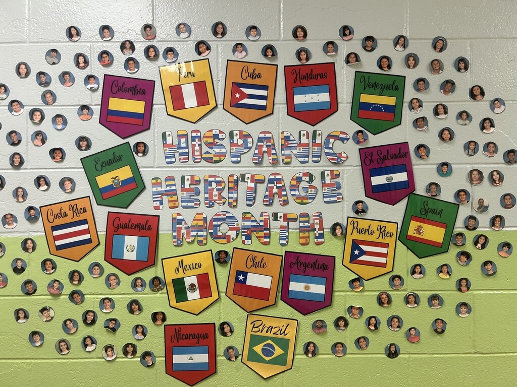 A classroom wall features a display celebrating Hispanic Heritage Month. It includes flags from various Hispanic countries and a central banner.