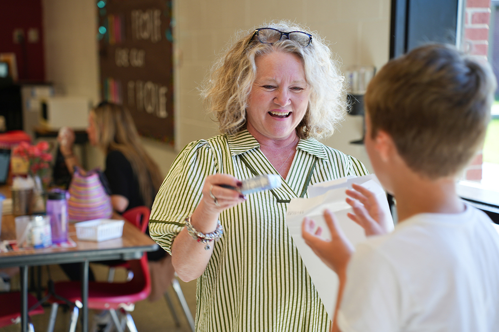 A woman smiling holds a toothbrush and a paper. A boy with short hair looks at her.
