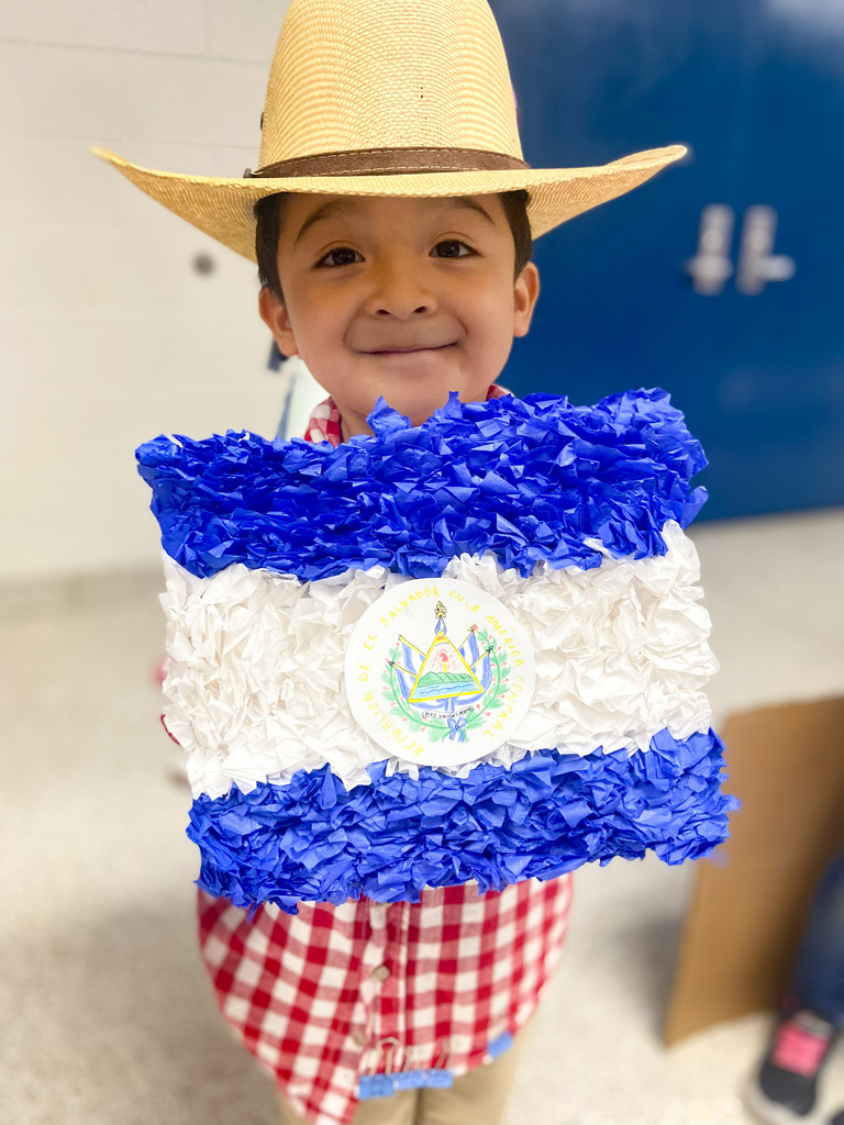 A child wears a cowboy hat and holds a blue and white paper craft with an emblem.