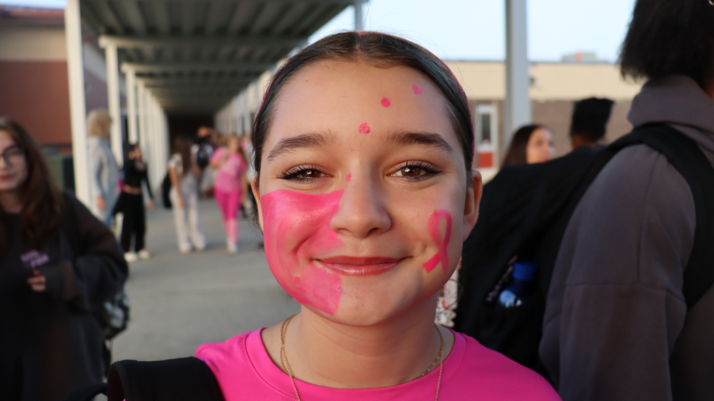 Girl with face painted pink in a school corridor, smiling for a picture with other students.