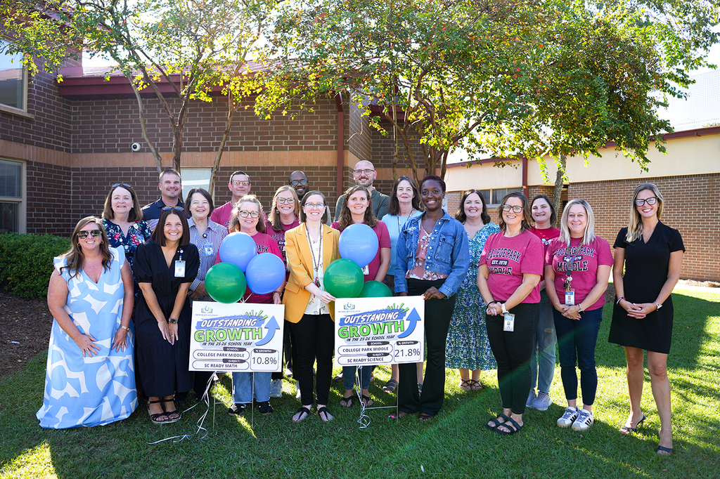 Group of adults with signs, balloons, and flags standing outside a school building.
