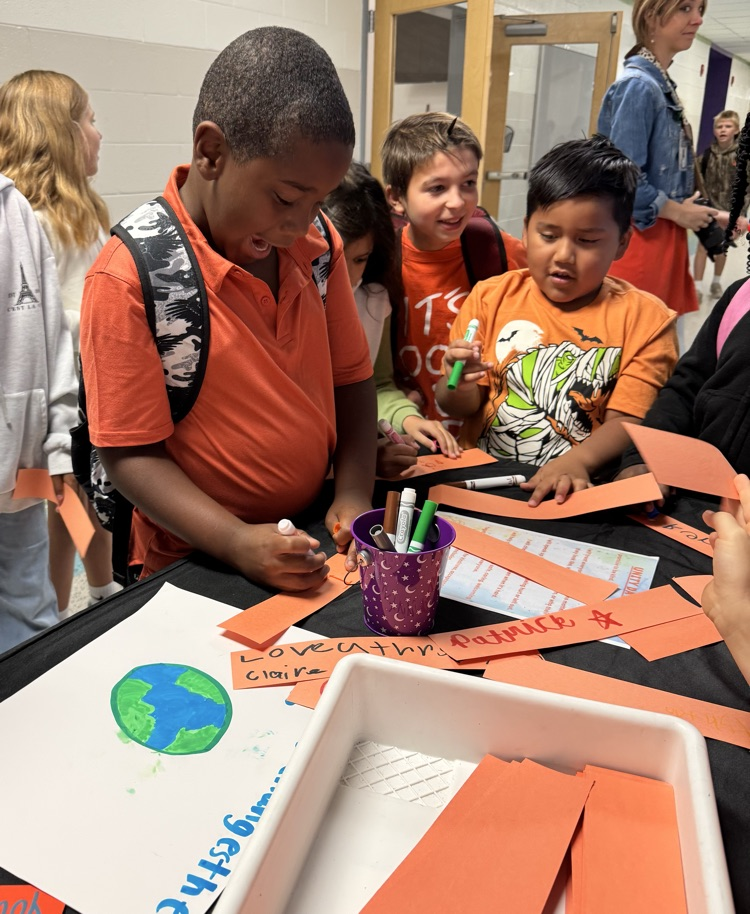 Children in a classroom engage with a project at a table. One boy draws on paper.