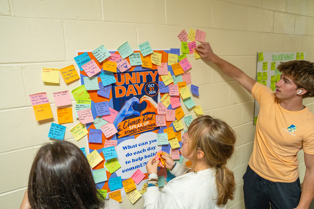 Three students standing in front of a bulletin board covered with colorful post-it notes.