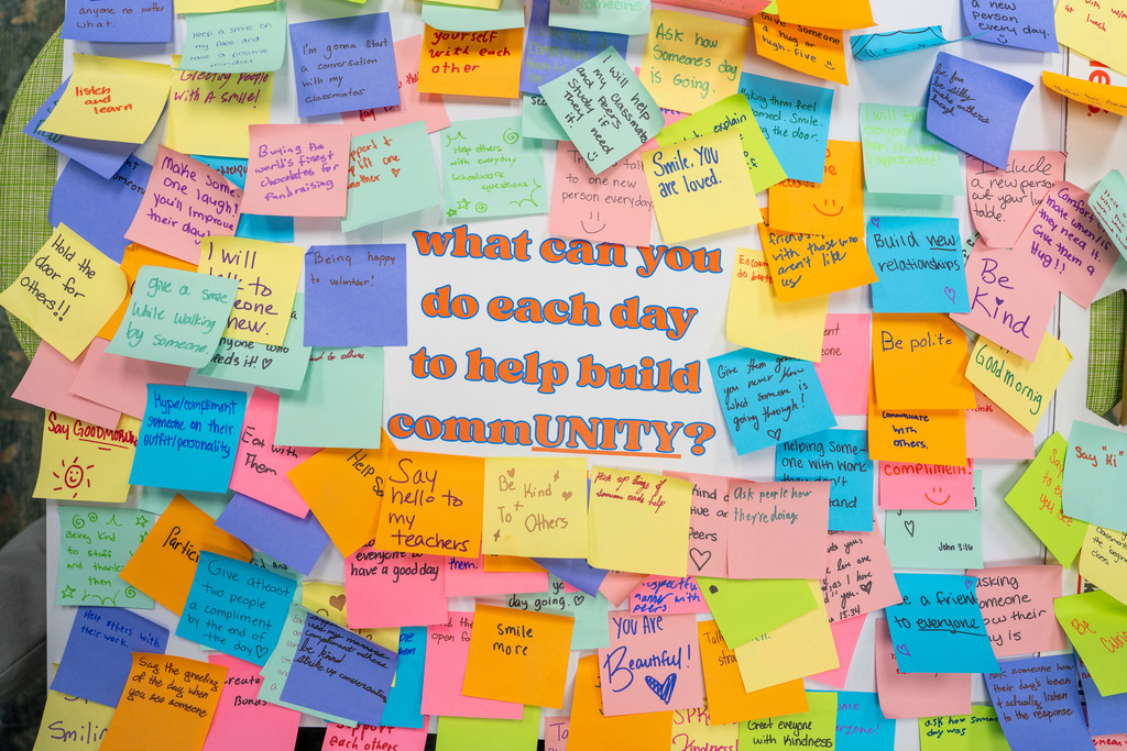 Multiple colorful sticky notes on a bulletin board with the question "What can you do each day to help build community?"