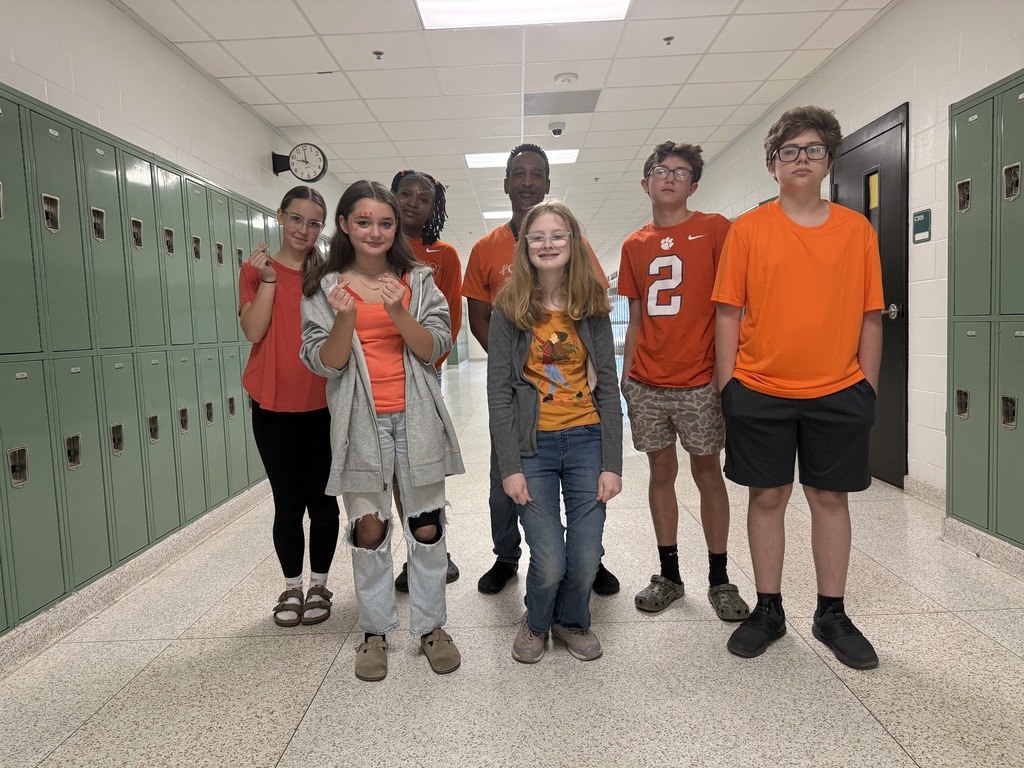 A group of children in orange and other shirts posing for a photo in a hallway.