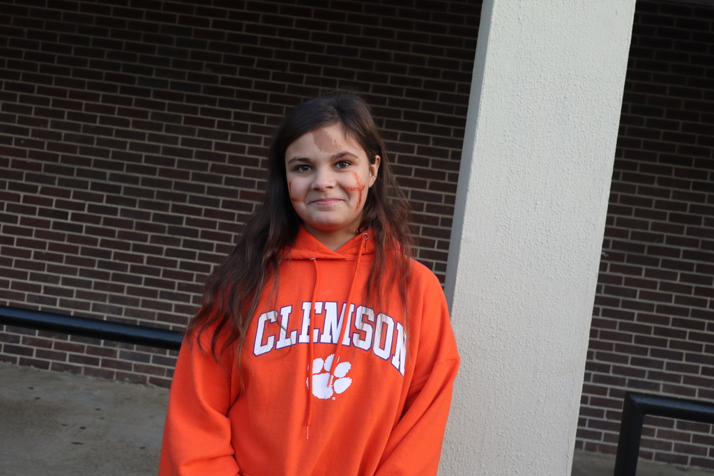 A young person stands outside by a brick wall, wearing a hoodie with "Clemson" on it.