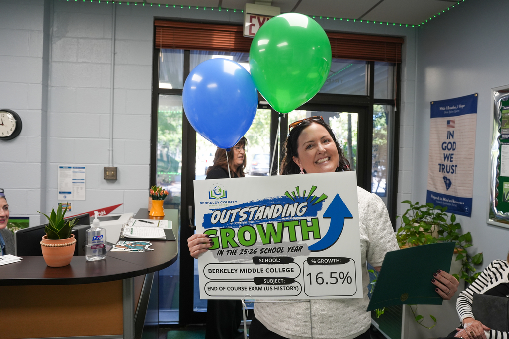 A woman holds a sign with green arrow and "OUTSTANDING GROWTH" text, and two balloons. Behind her, a desk with potted plant, clock, and a bulletin board.