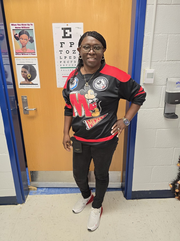 Adult woman in black and red sports jersey with Mickey Mouse logo, wearing glasses, standing in a classroom.
