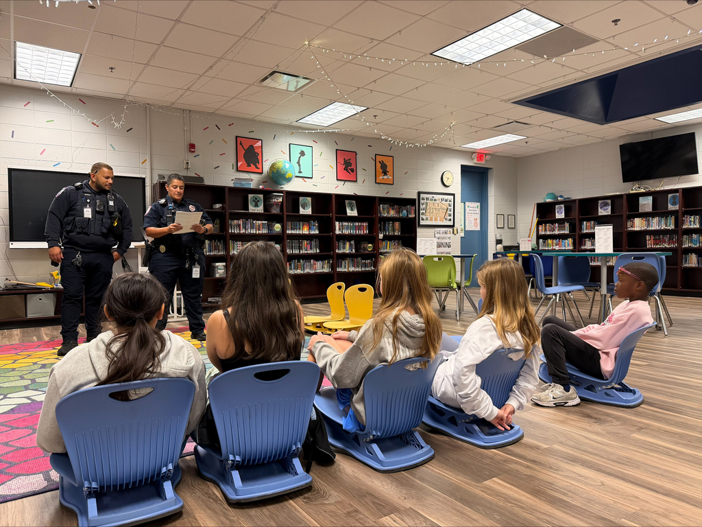 A police officer standing with a book while a group of students sit on chairs and listen.
