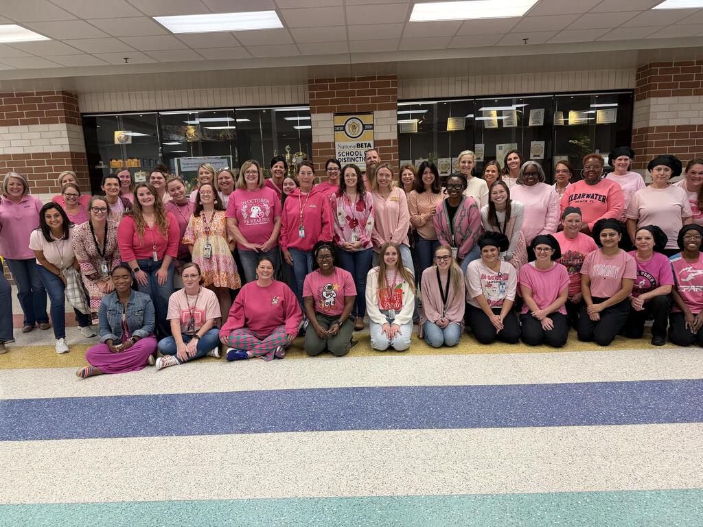 Large group of people in pink shirts posing for a photo in a school hallway.