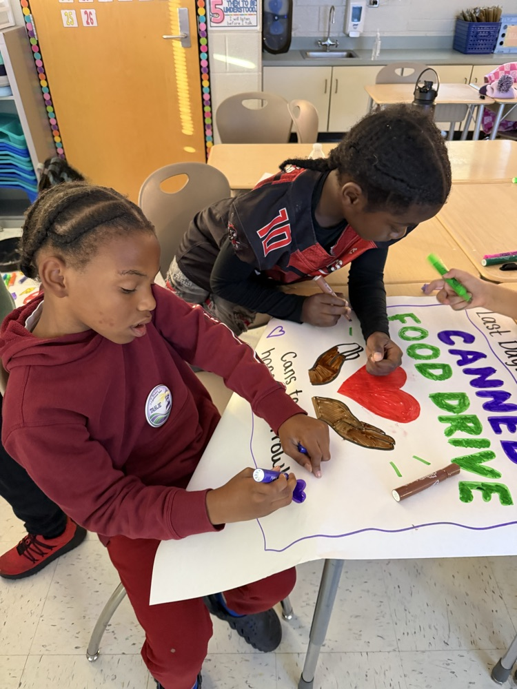 Two students coloring a large sign with a banner that says "Food Canned Drive" and other words.