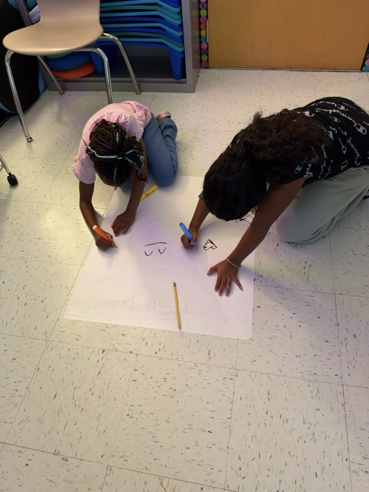 Two children on floor, drawing numbers on a white sheet of paper with markers.