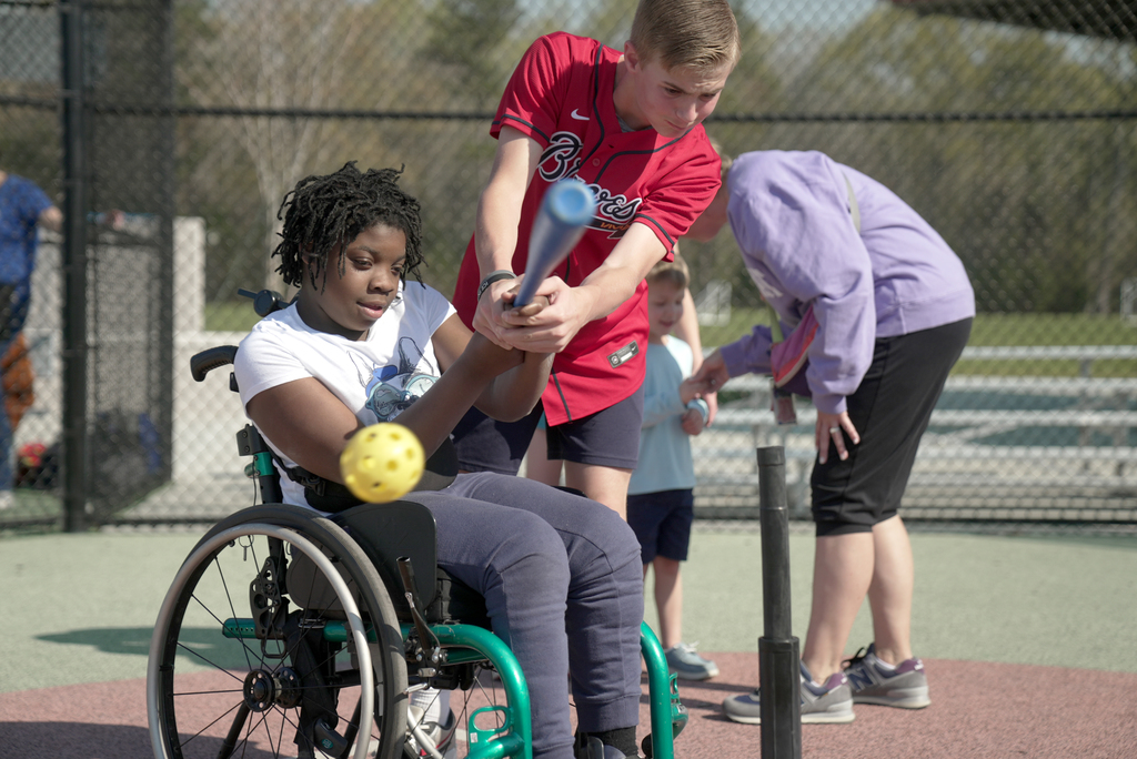 kid in wheelchair hitting a baseball with the help of another student