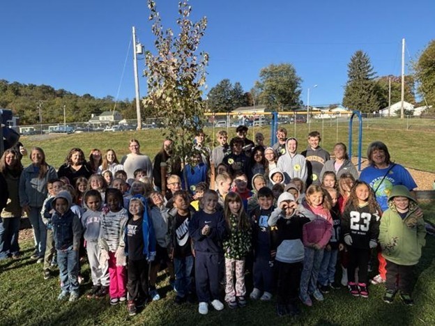 Students, teachers and volunteers gather in front of a newly planted tree at Hedgesville Elementary School.