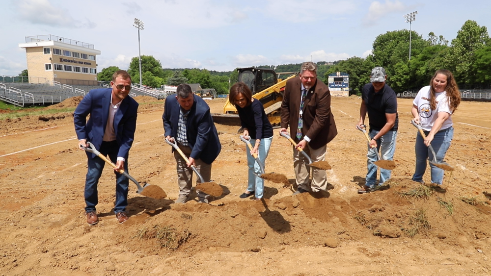 image if people scooping up dirt with a shovel at a groundbreaking ceremony for hedgesville high school's new turf field