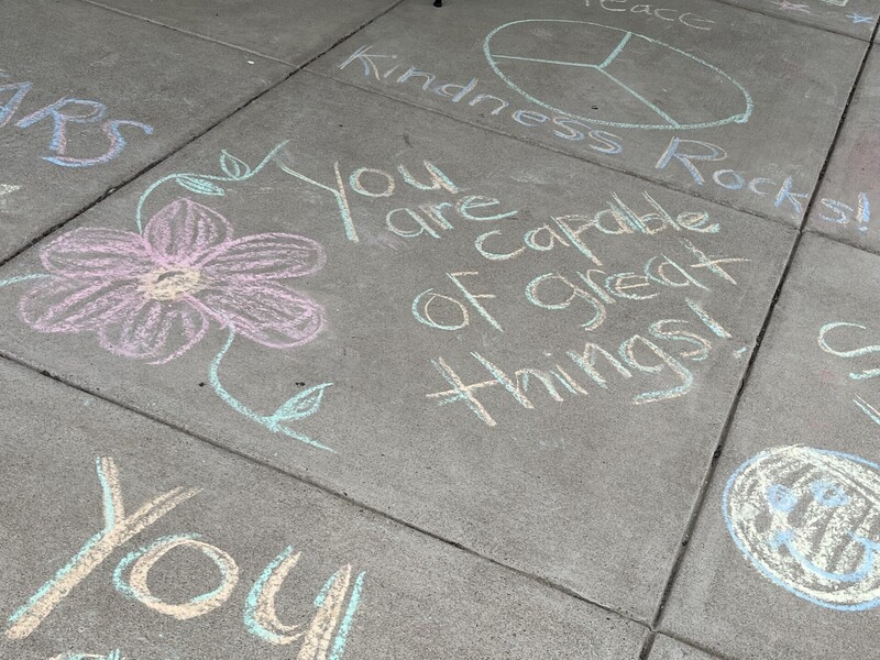 Chalk words on the sidewalk on the first day of school. One says "You are capable of great things!"